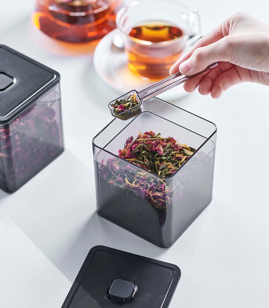 View 11 - Person scooping tea leaves with spoon from black Vacuum-Sealing Food Container by Yamazaki Home.