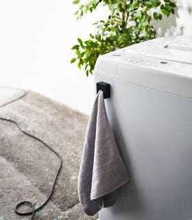 Black Yamazaki Home Traceless Adhesive Towel Holder attached to a washing machine with a towel inserted view 16