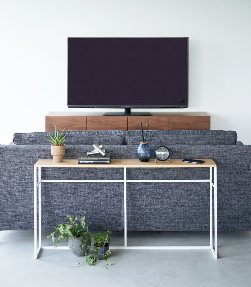 Straight view of the Long Console Table by Yamazaki Home in white with decorative items placed behind a gray couch in a living room.