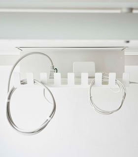 Under-Desk Cable Organizer in white by Yamazaki Home mounted under a desk holding cables. view 6