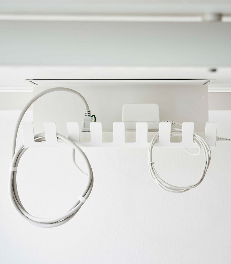 View 6 - Under-Desk Cable Organizer in white by Yamazaki Home mounted under a desk holding cables.