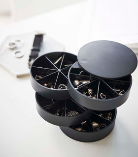A profile view of the inside contents of a black cylinder-shaped four-tier swivel accessory holder. The accessory holder’s tiers and lid are swiveled opened so the inside contents can be seen. Each tier of the accessory holder is divided into seven separate compartments in a pie-chart fashion. view 23