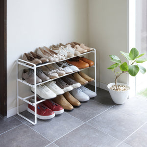 White 3-Tier Expandable Shoe Rack in entryway holding shoes by Yamazaki Home.