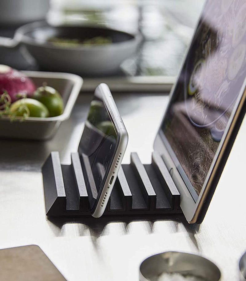 Side view of black Phone and Tablet Stand holding phone and tablet on kitchen countertop by Yamazaki Home.