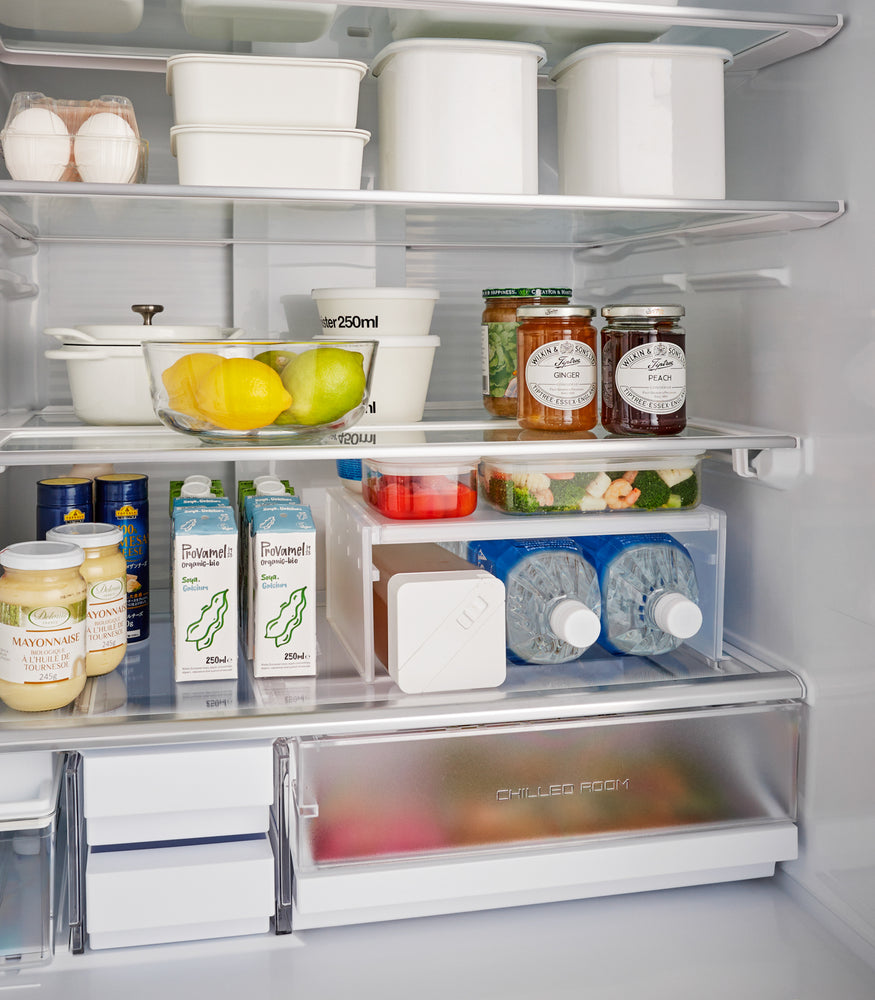 View 2 - A white Expandable Refrigerator Riser Shelf by Yamazaki Home displayed in an open fridge, holding food items, demonstrating space utilization.