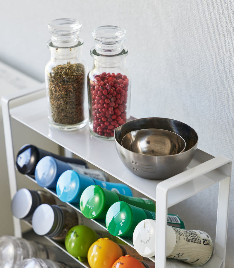 Close-up of a White Four-Tier Slim Spice Rack by Yamazaki Home with spices, oils, and cooking utensils on a kitchen counter.