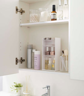 A white medicine cabinet is open to display the inside contents. Sunlight is focused on the right upper corner. Below is a bathroom sink. view 22