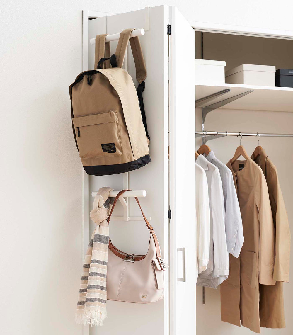 White Kids' Backpack Hanger holding a backpack, scarf, and purse on closet door by Yamazaki Home.