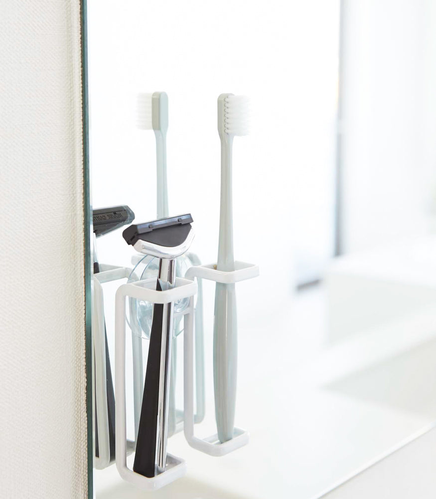 View 2 - White Toothbrush Holder holding toothbrush and razor in bathroom by Yamazaki Home.