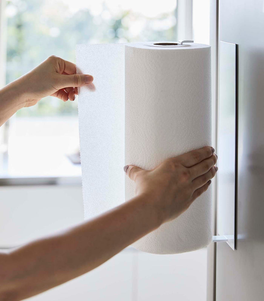 View 6 - Side view of person grabbing paper towel from White Magnetic Paper Towel Holder by Yamazaki Home.