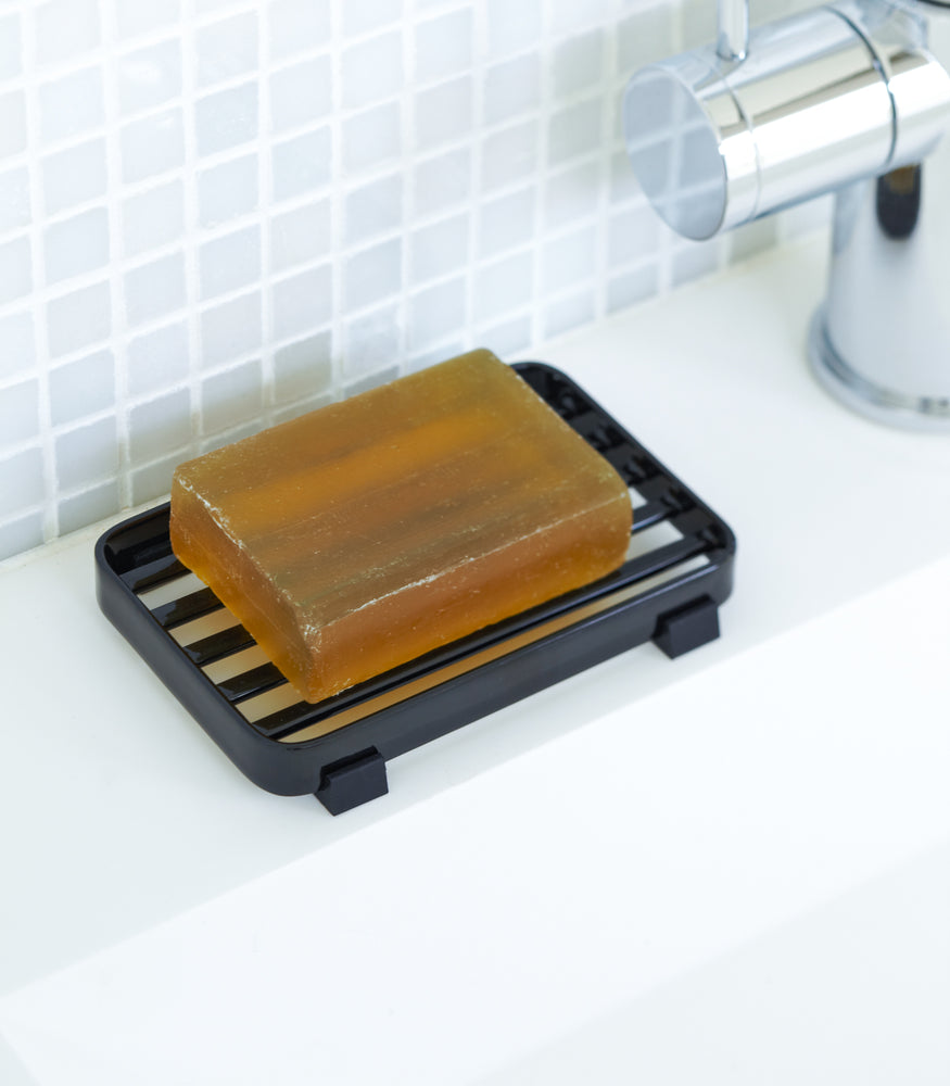 View 6 - Black Slotted Soap Tray holding soap bar on sink counter by Yamazaki Home.