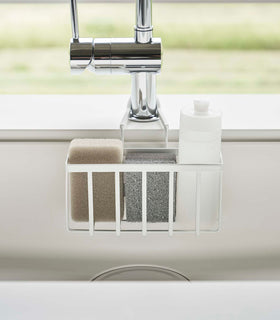 Close up frontal view of a Yamazaki Home white Faucet-Hanging Sponge Caddy in a sink view 4