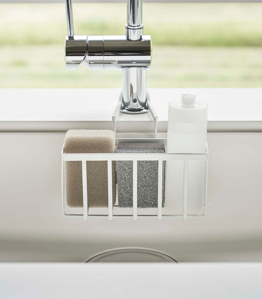 View 4 - Close up frontal view of a Yamazaki Home white Faucet-Hanging Sponge Caddy in a sink