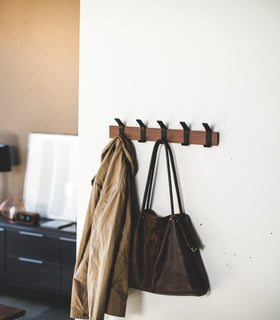 Walnut Wall-Mounted Coat Hanger holding bag and coat by Yamazaki Home. view 7