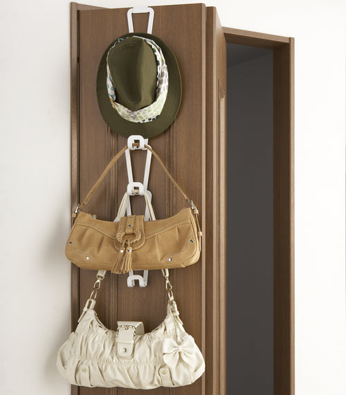 Front view of white Chain Link Bag Hanger holding purses and hat on closet door by Yamazaki Home.