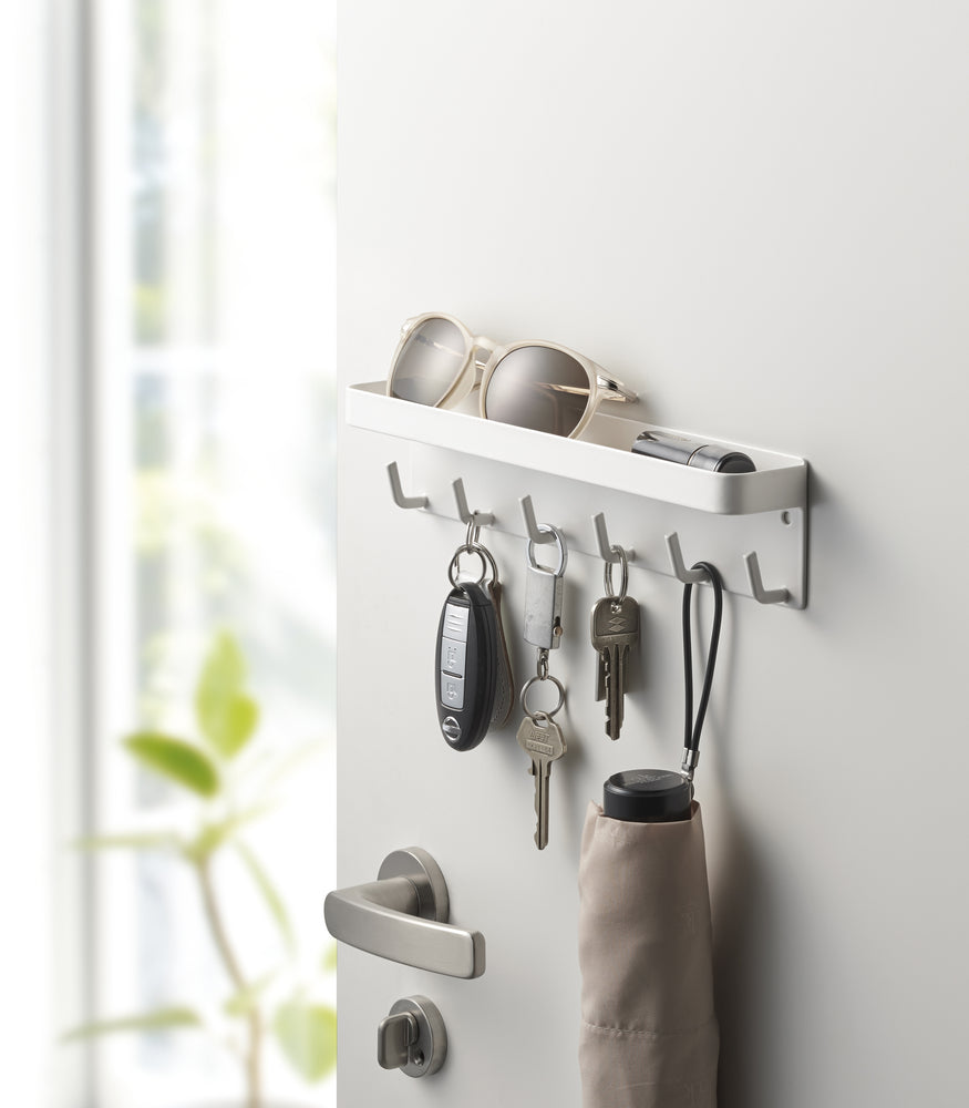 View 2 - White Magnetic Key Rack with Tray holding keys, umbrella, and sunglasses on door by Yamazaki Home.