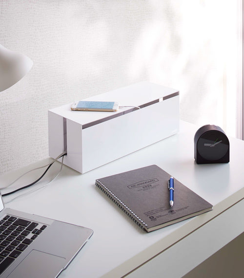 White Cable Management Box holding charging cords on office desk by Yamazaki Home.