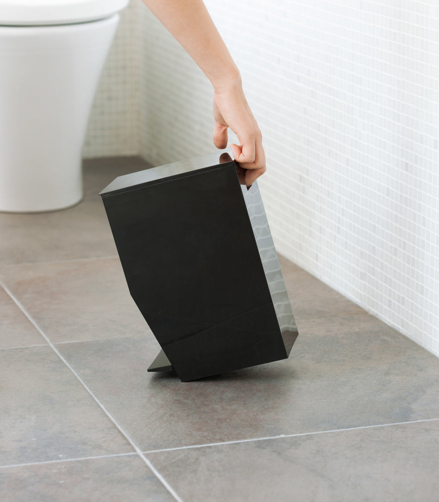 View 12 - Side view of black Step Trash Can held by handle in bathroom by Yamazaki Home.