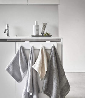 Front view of white Push Dish Towel Holder holding hand towels on bathroom sink cabinet by Yamazaki Home. view 4