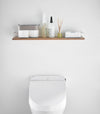 Front view of Wall-Mounted Shelf holding bathroom accessories in bathroom by Yamazaki Home.