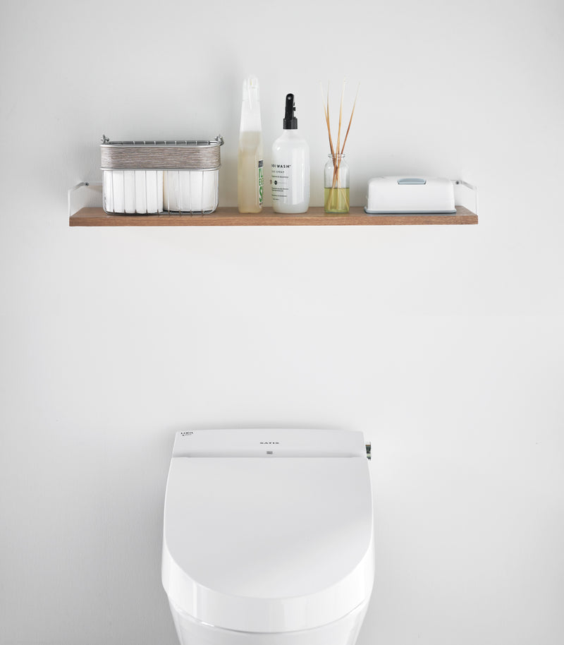 Front view of Wall-Mounted Shelf holding bathroom accessories in bathroom by Yamazaki Home.