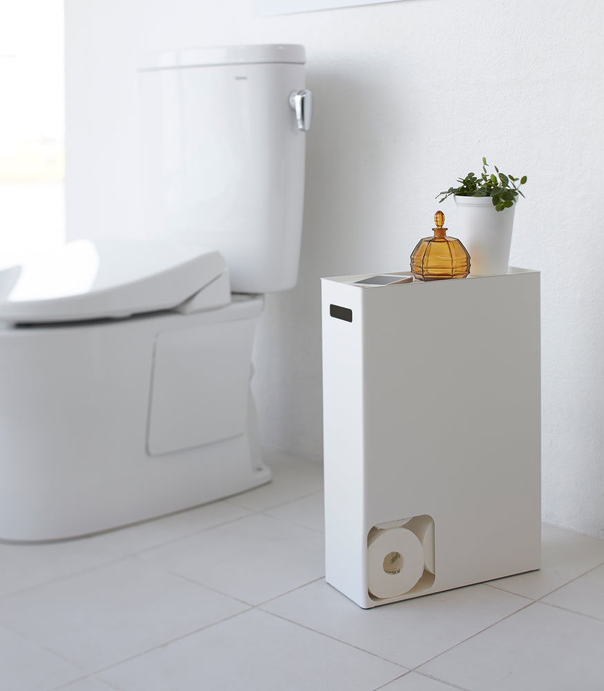 View 3 - Side view of white Toilet Paper Stocker displaying phone and plant in bathroom by Yamazaki Home.