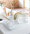 Front view of white Dish Rack holding plates, cups, and silverware on kitchen counter by Yamazaki Home.