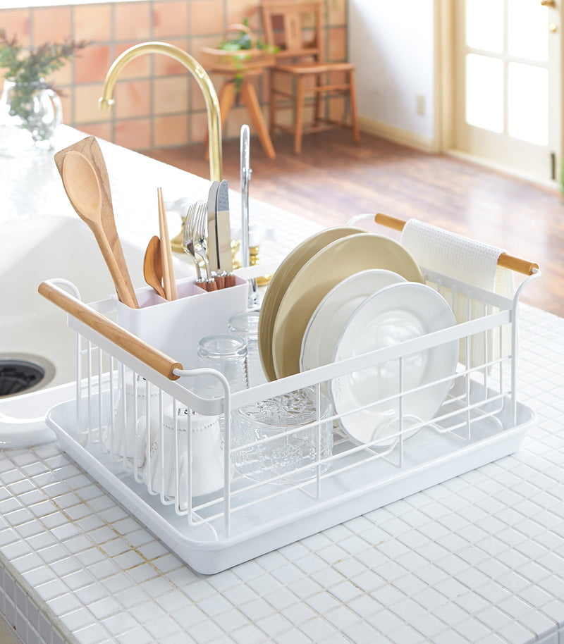 Front view of white Dish Rack holding plates, cups, and silverware on kitchen counter by Yamazaki Home.