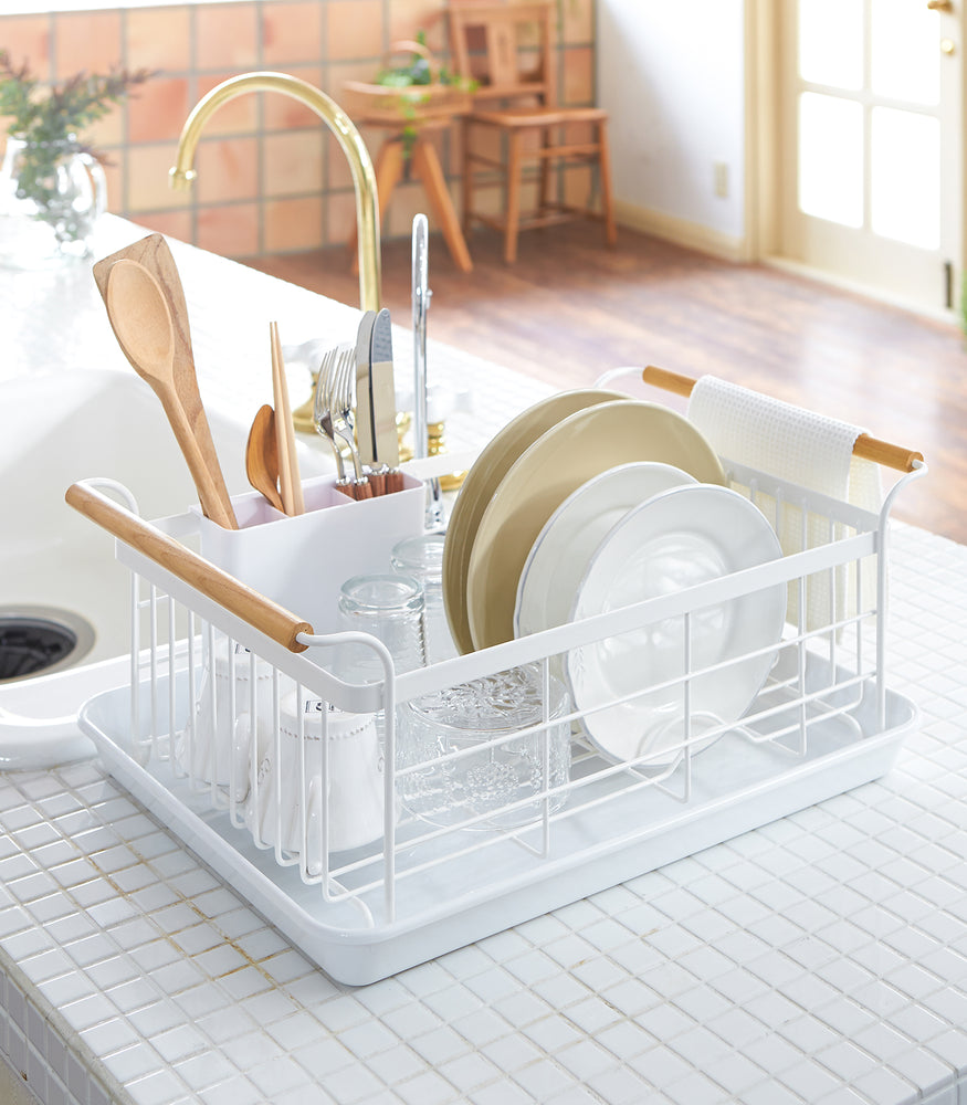 View 3 - Front view of white Dish Rack holding plates, cups, and silverware on kitchen counter by Yamazaki Home.