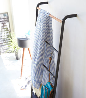 Angled side view of black Leaning Ladder Rack holding clothing items and accessories by Yamazaki Home. view 7