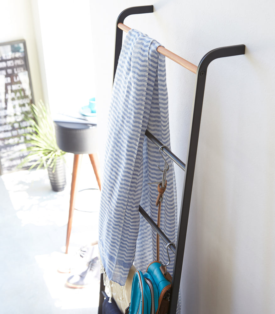 View 7 - Angled side view of black Leaning Ladder Rack holding clothing items and accessories by Yamazaki Home.
