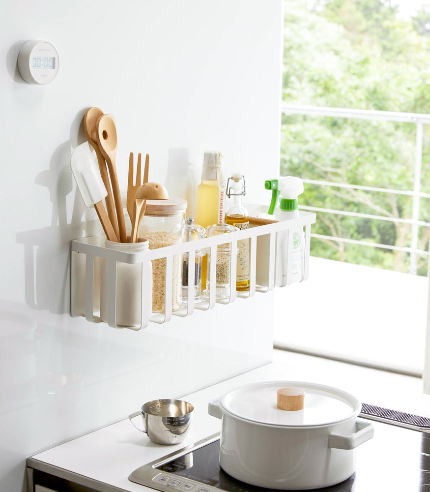 View 3 - White Magnetic Storage Basket holding spices, oils, and cooking utensils in kitchen by Yamazaki Home.