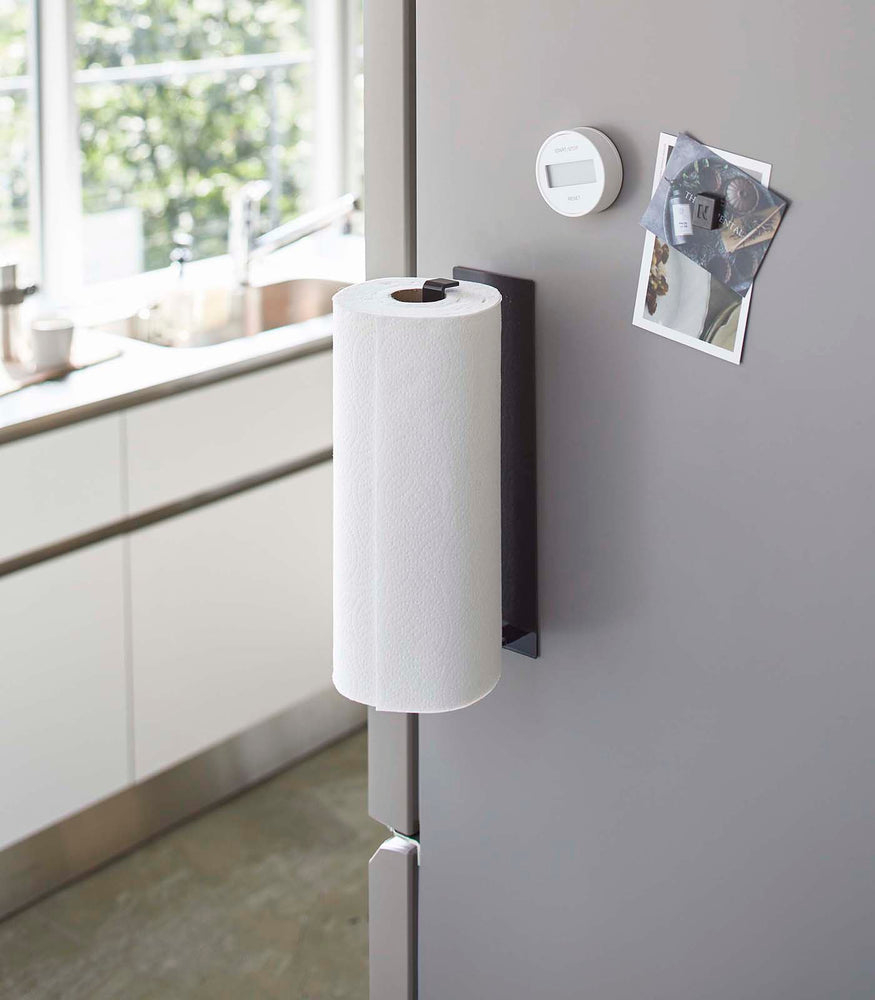 View 9 - Black Magnetic Paper Towel Holder holding dish towel on kitchen fridge by Yamazaki Home.