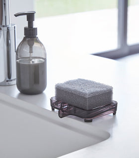 Black Self-Draining Soap Tray holding sponge on sink counter by Yamazaki Home. view 8
