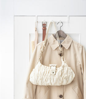 Front view of white Over-the-Door Hanger on door hanging purse, belt, brush, and jacket by Yamazaki Home. view 3