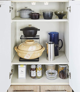 Front view of black 2-Tier Pot Holder with Hooks holding pots in kitchen cabinet by Yamazaki Home. view 10