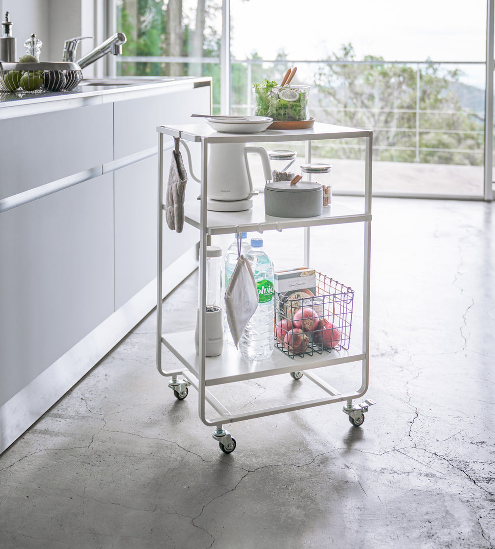 White Rolling Utility Cart holding food and kitchen supplies in kitchen by Yamazaki Home.
