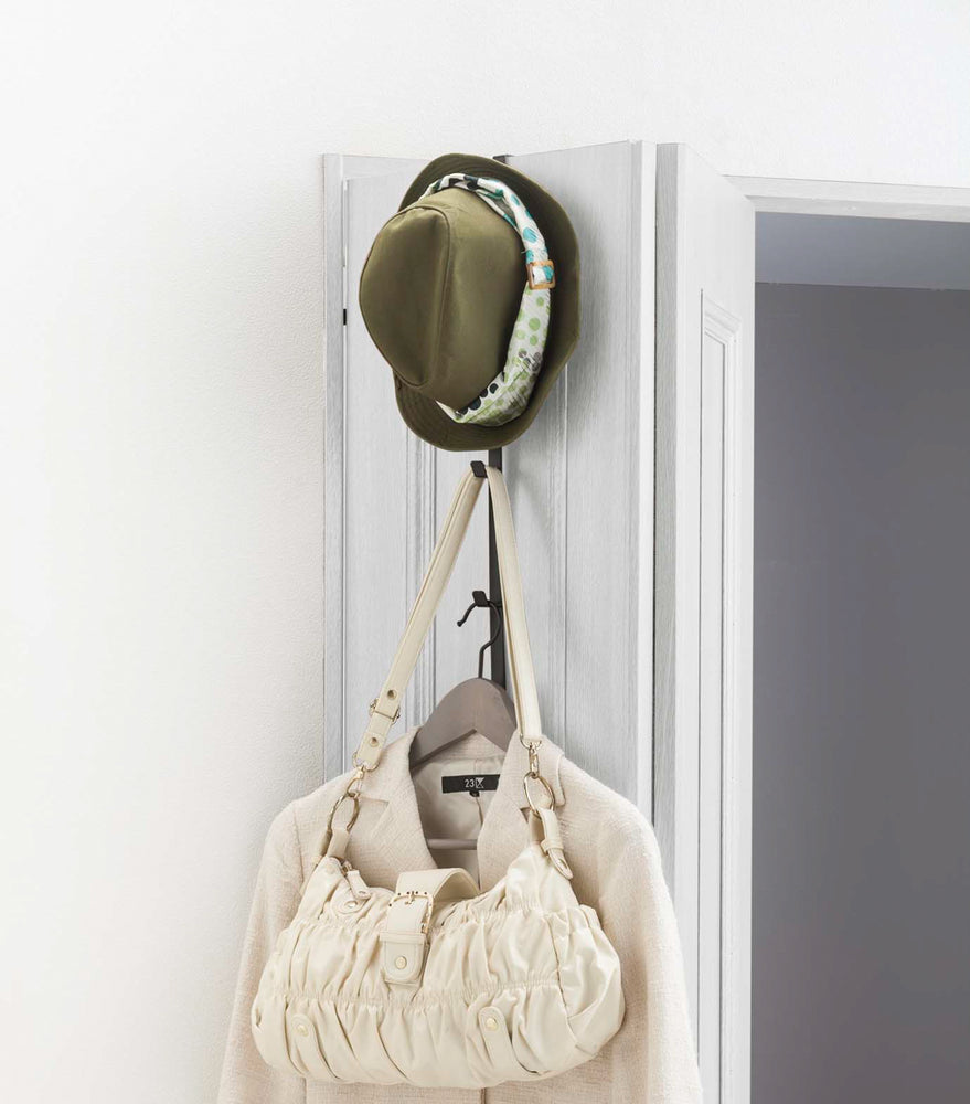 View 9 - Black Over-the-Door Hanger holding hat, purse, and jacket on closet door by Yamazaki Home.