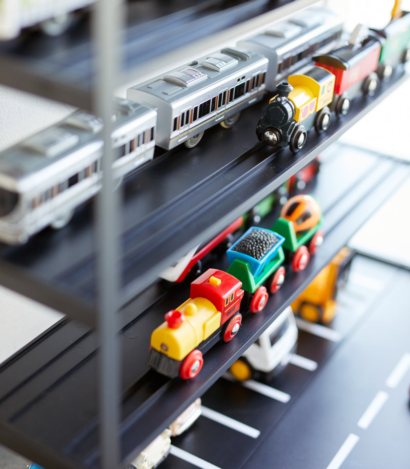 Close up view of black Kid's Parking Garage shelving holding toy trains by Yamazaki Home.
