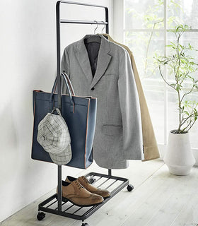 Black Rolling Coat Rack holding jackets, bag, hat, and shoes by Yamazaki Home. view 10