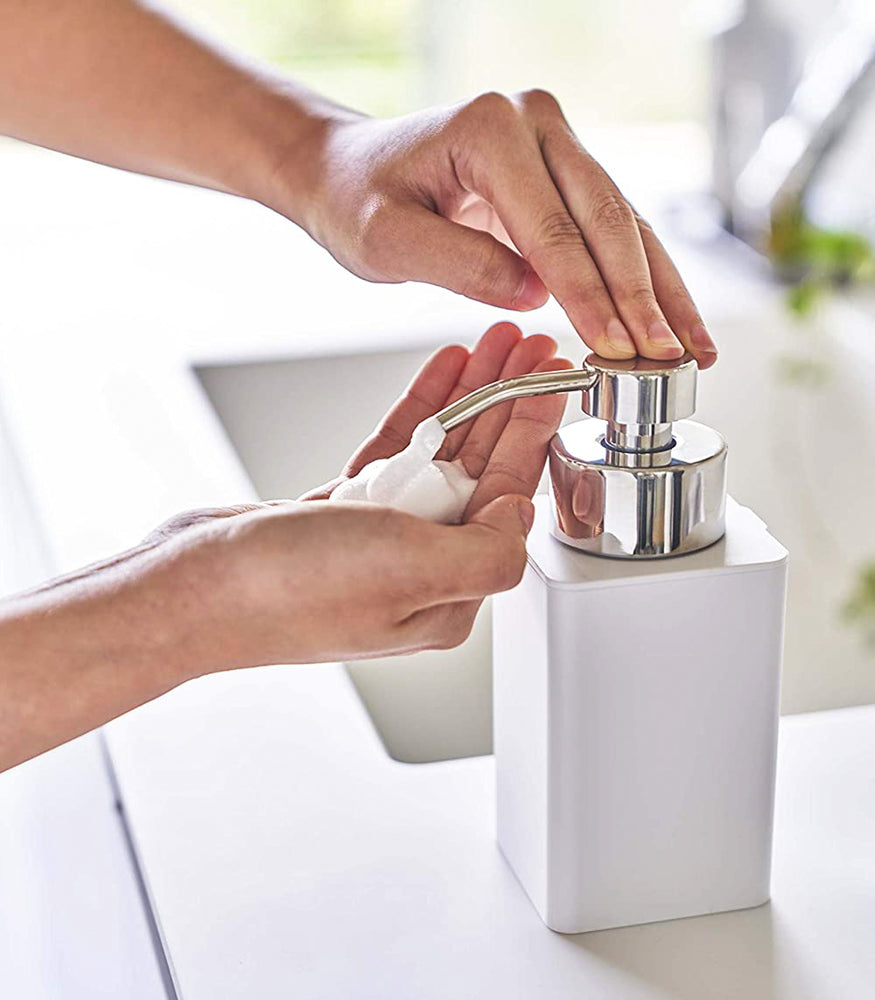 View 3 - White Foaming Soap Dispenser dispensing soap on bath countertop by Yamazaki Home.