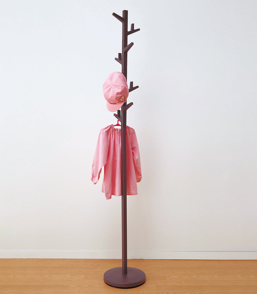 View 10 - Yamazaki's Brown coat rack in the shape of a tree, hung with pink children's clothes.
