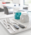 Closeup view of white Dish Drainer Tray holding silverware and glasses by Yamazaki Home.