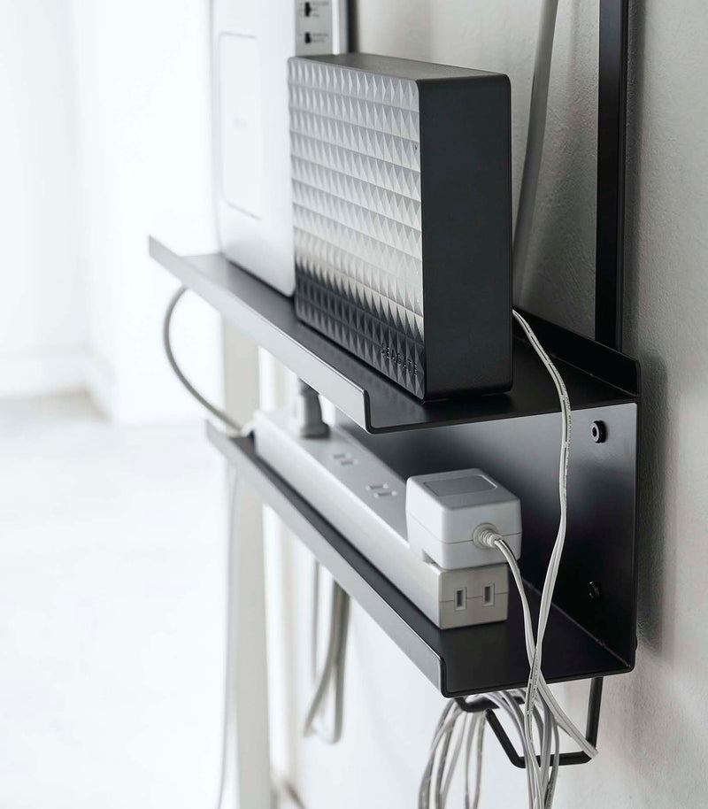 Side view of black Wall-Mount Cable and Router Storage Rack holding routers and power cord by Yamazaki Home.