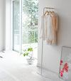 White Slim Leaning Coat Rack holding dresses and blouse by Yamazaki Home.