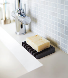 Black Self-Draining Soap Tray holding soap on sink counter by Yamazaki Home. view 6