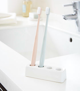 Front Ceramic Toothbrush Stand holding toothbrushes on bathroom counter by Yamazaki Home. view 2