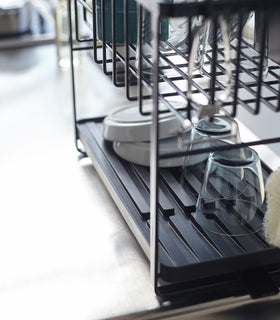 Close up of black Two-Tiered Dish Rack bottom rack holding plates and cups by Yamazaki Home. view 14