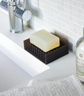 Black Self-Draining Soap Dish holding soap bar on sink counter by Yamazaki Home. view 5