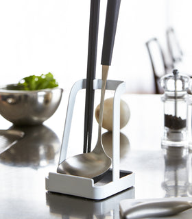 White Lid & Ladle Stand holding ladle and tongs on kitchen counter by Yamazaki Home. view 4
